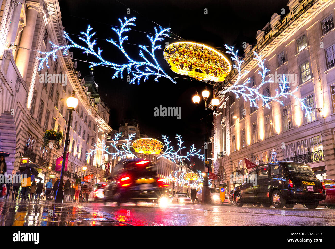 CHRISTMAS SHOPPING REGENT STREET LONDON belebte Szene von Weihnachten Shopper in Regen, traditionellen schwarzen Taxis, Verkehr und Sonnenschirme in einem feuchten reflektierende Regent Street mit Weihnachtsbeleuchtung über und hinter London UK Stockfoto