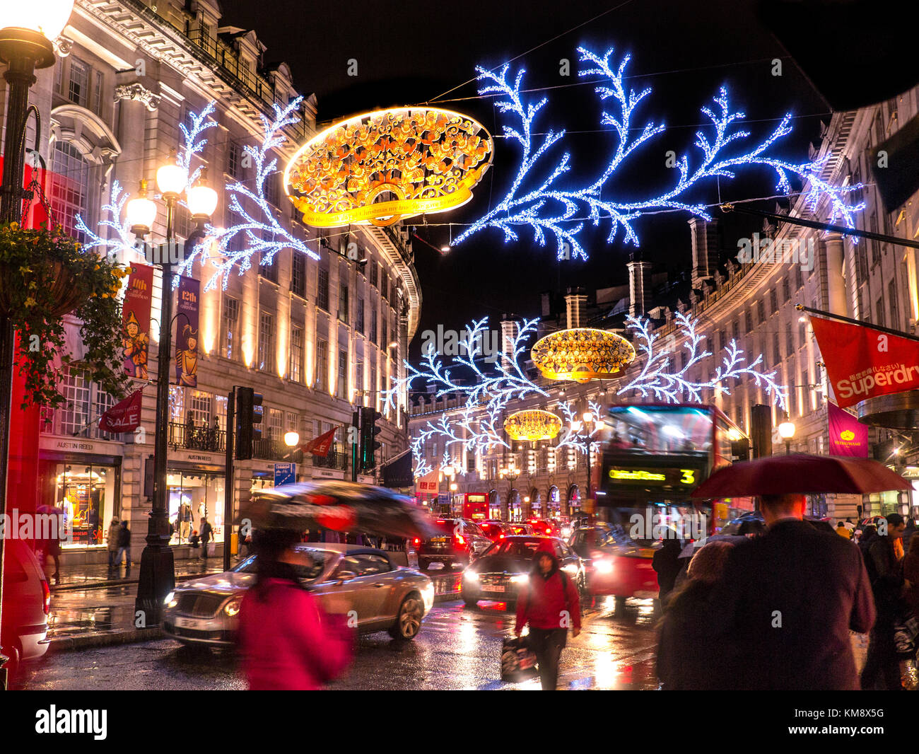 WEIHNACHTSVERKÄUFE SHOPPING LONDONER SZENE REGNET REGENT STRASSENLATERNEN LONDONER NACHT geschäftige Actionszene Weihnachtseinkäufer, verschwommener Verkehr und Regenschirme in einer regnerischen, nassen, glänzenden Regent Street mit Weihnachtslichtern über und hinter London UK Stockfoto