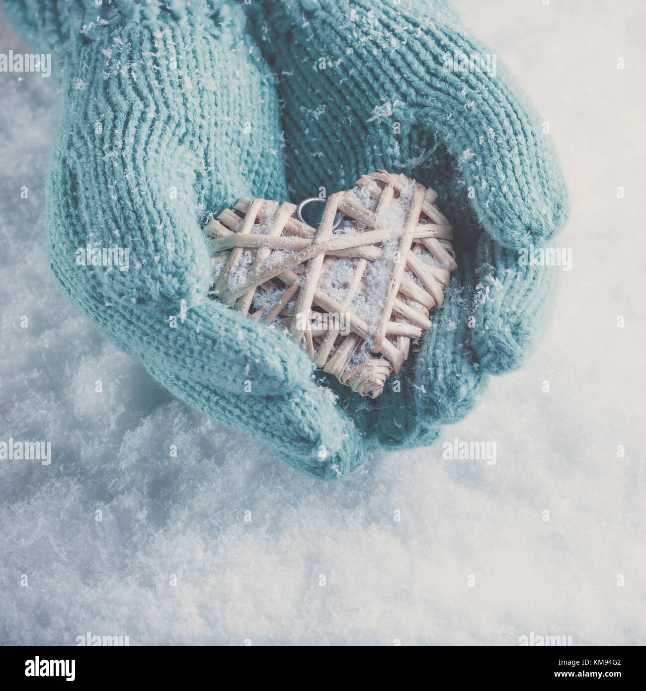 Frau Hände in Light teal Gestrickte Handschuhe halten einen schönen Herzen im Schnee Hintergrund. Liebe und st. Valentin Konzept. instagram Wirkung. Stockfoto