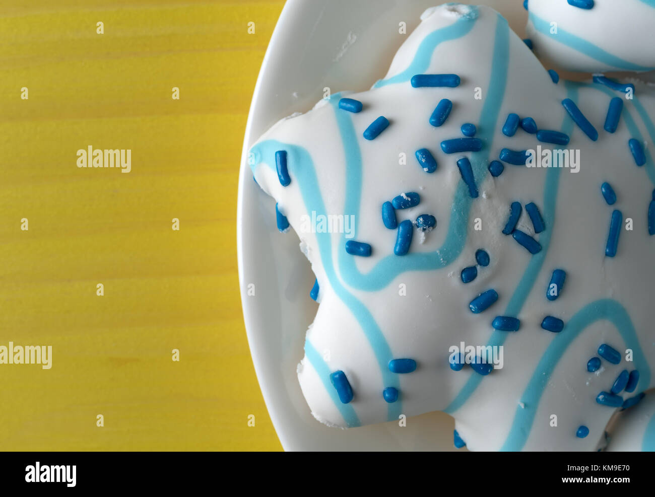 Oben in der Nähe der großen blauen und weißen Farben sternförmigen Weihnachtsplätzchen auf einem weißen Teller auf einem Gelb lackiert Tischplatte. Stockfoto