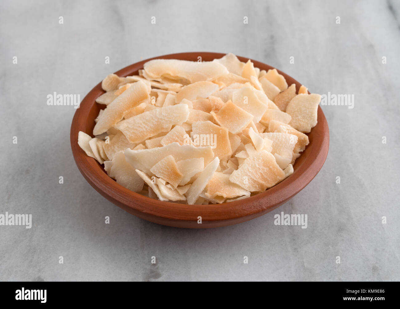 Eine kleine terracotta Schale mit gerösteten Kokosflocken auf grauem Marmor Zähler nach oben gefüllt. Stockfoto