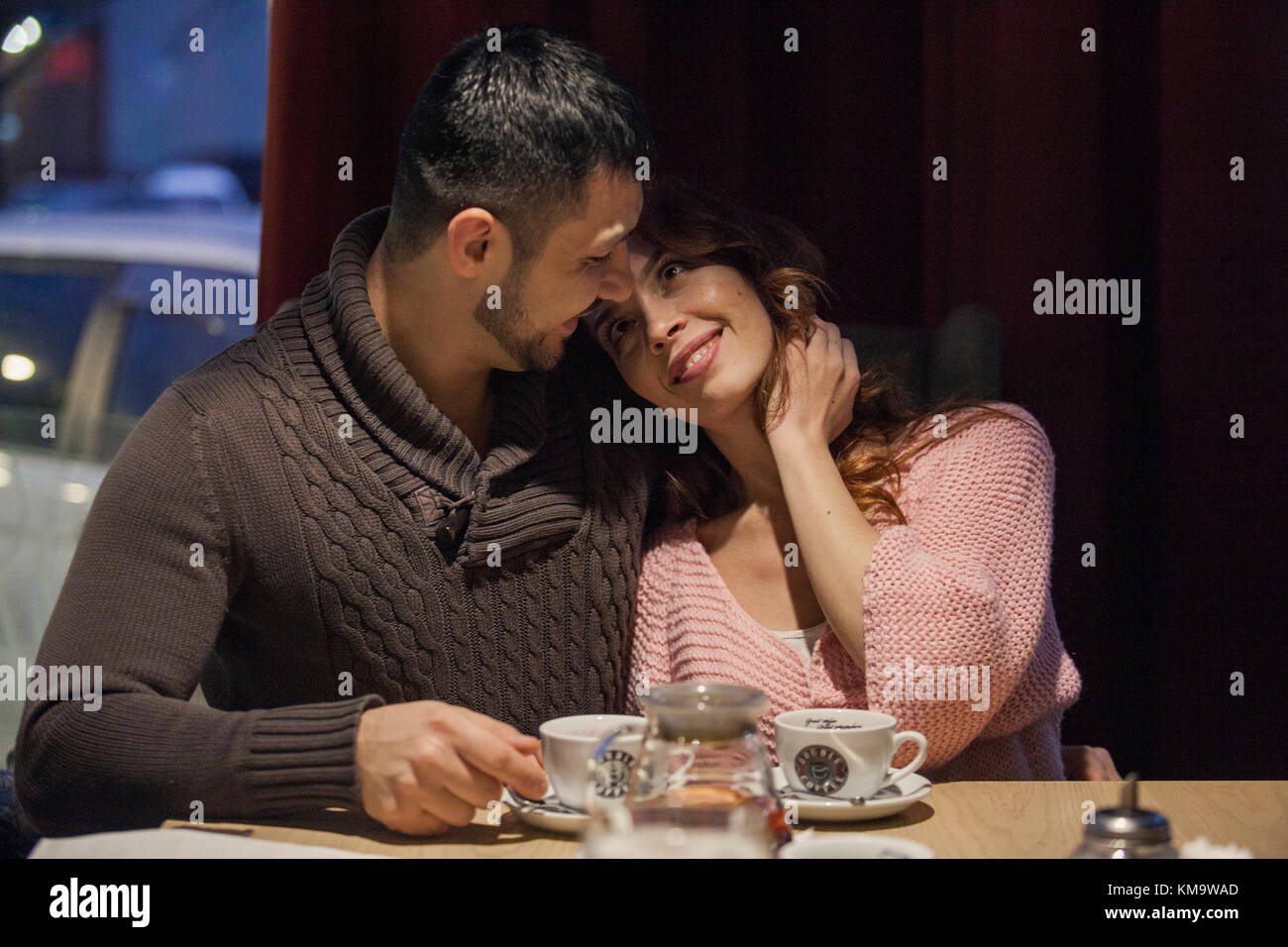 Paar durch ein Fenster auf lokaler Kaffee Platz und genießen winter nacht mit heißen Getränken und beiläufiges Gespräch. Schuss von aussen durch den Wind Stockfoto