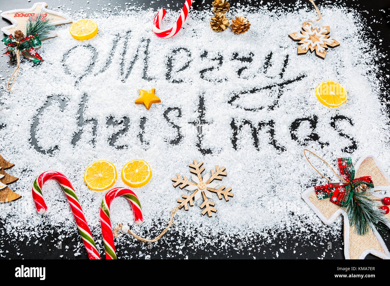Weihnachten Hintergrund mit der Aufschrift frohe Weihnachten auf weißem Schnee mit Holzspielzeug, Zitrone, Süßigkeiten, Schneeflocken und neues Jahr Dekor. Winterurlaub Stockfoto