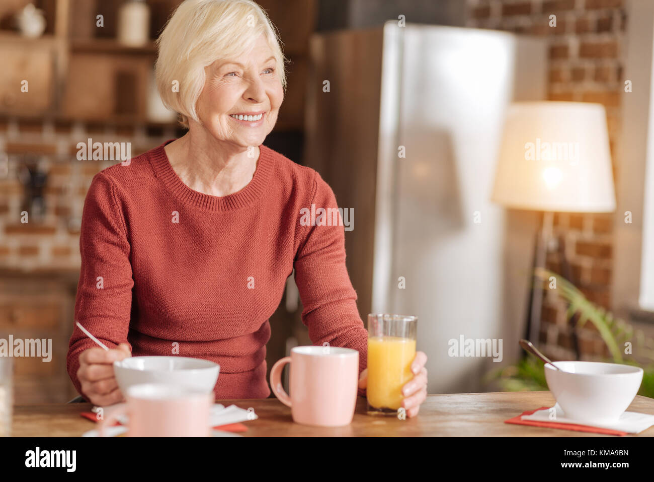 Freundliche ältere Frau essen Frühstück und lächelnd Stockfoto