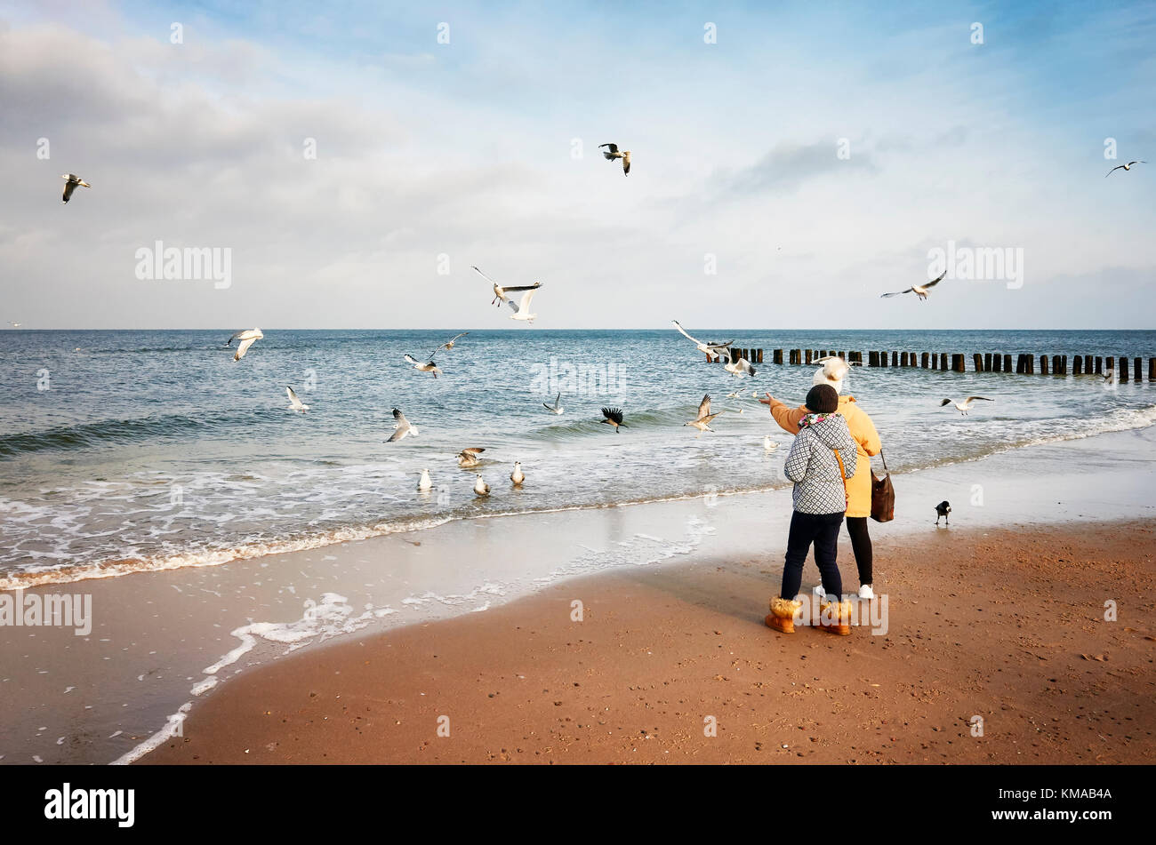 Dziwnowek, Polen - Dezember 03, 2017: Zwei Frauen feed Vögel am Strand an einem kalten Tag. Stockfoto