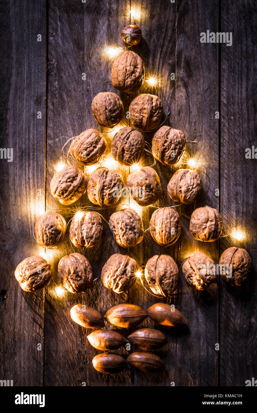 Walnüsse und Pekannuss auf einer hölzernen Hintergrund in eine Weihnachtsbaum Form mit Golden Lights unter die Völker zerstreut angeordnet. Stockfoto