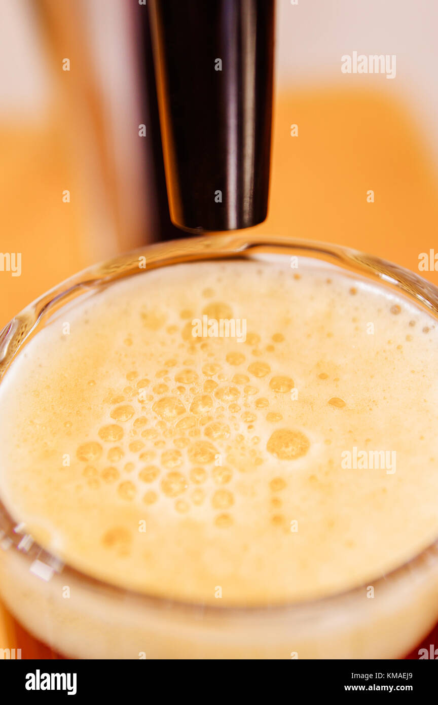 Nahaufnahme von einem Glas Bier mit Schaum und Bier zapfen, Bier in einem Restaurant oder Pub serviert, in einem verschwommenen Hintergrund Stockfoto