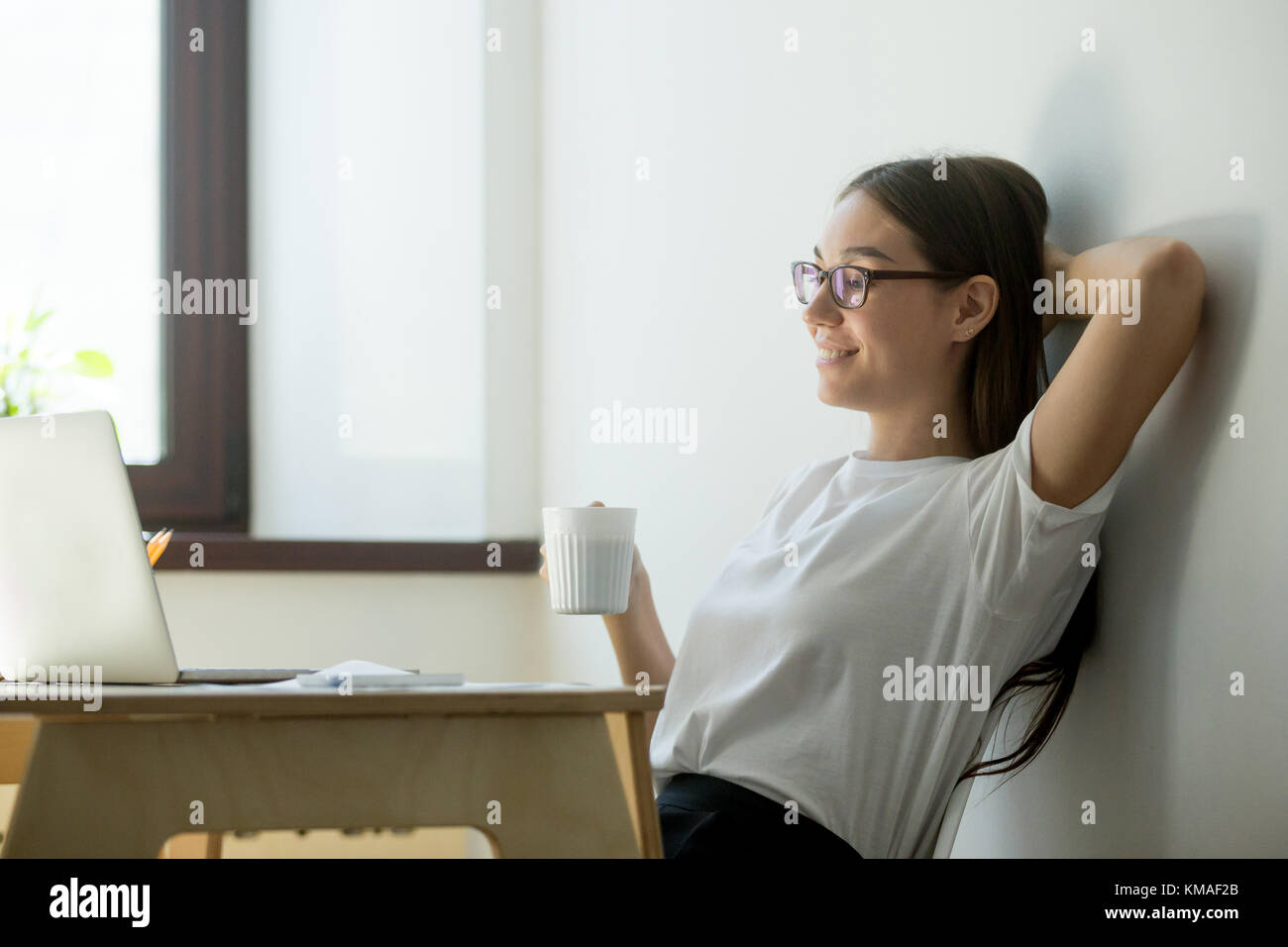 Zufriedene junge Geschäftsfrau, die Hand hinter den Kopf und trinkt Kaffee. Schöne weibliche Manager, Pause, Ruhe und lächelnd Stockfoto