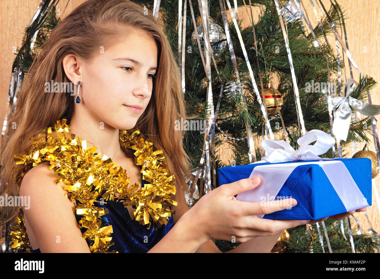 Schöne jugendlich Mädchen in der Nähe von Weihnachten Baum sieht glücklich auf Geschenk in ihren Händen Stockfoto