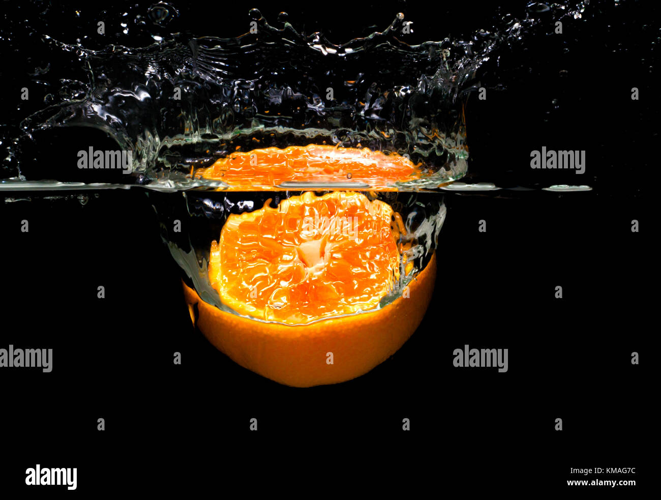 Cut orange in Spritzwasser fällt, auf schwarzem Hintergrund isoliert. Stockfoto