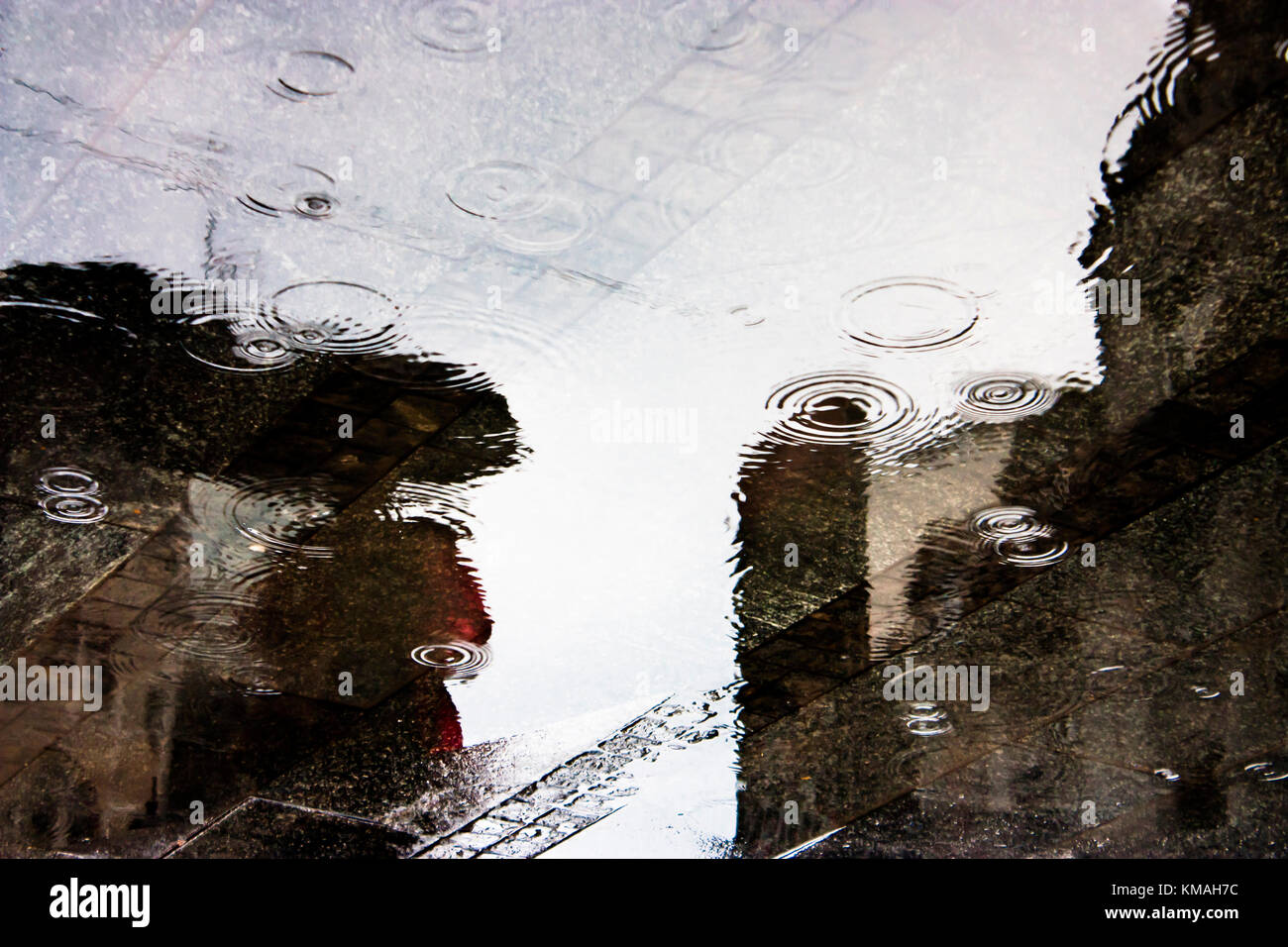 Blurry regen Reflexion silhouette Schatten einer Person, die unter dem Dach in einer Stadtstraße Pfütze mit Drop Wellen an einem regnerischen Tag Stockfoto