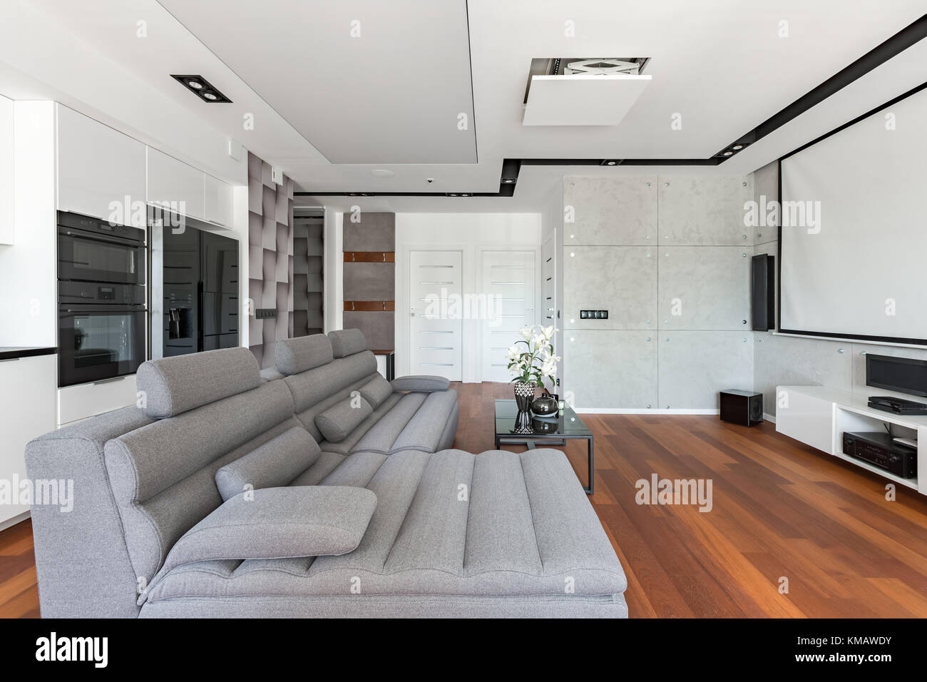 Modernes Wohnzimmer mit Projektionsleinwand, Sofa und Kochnische Stockfoto