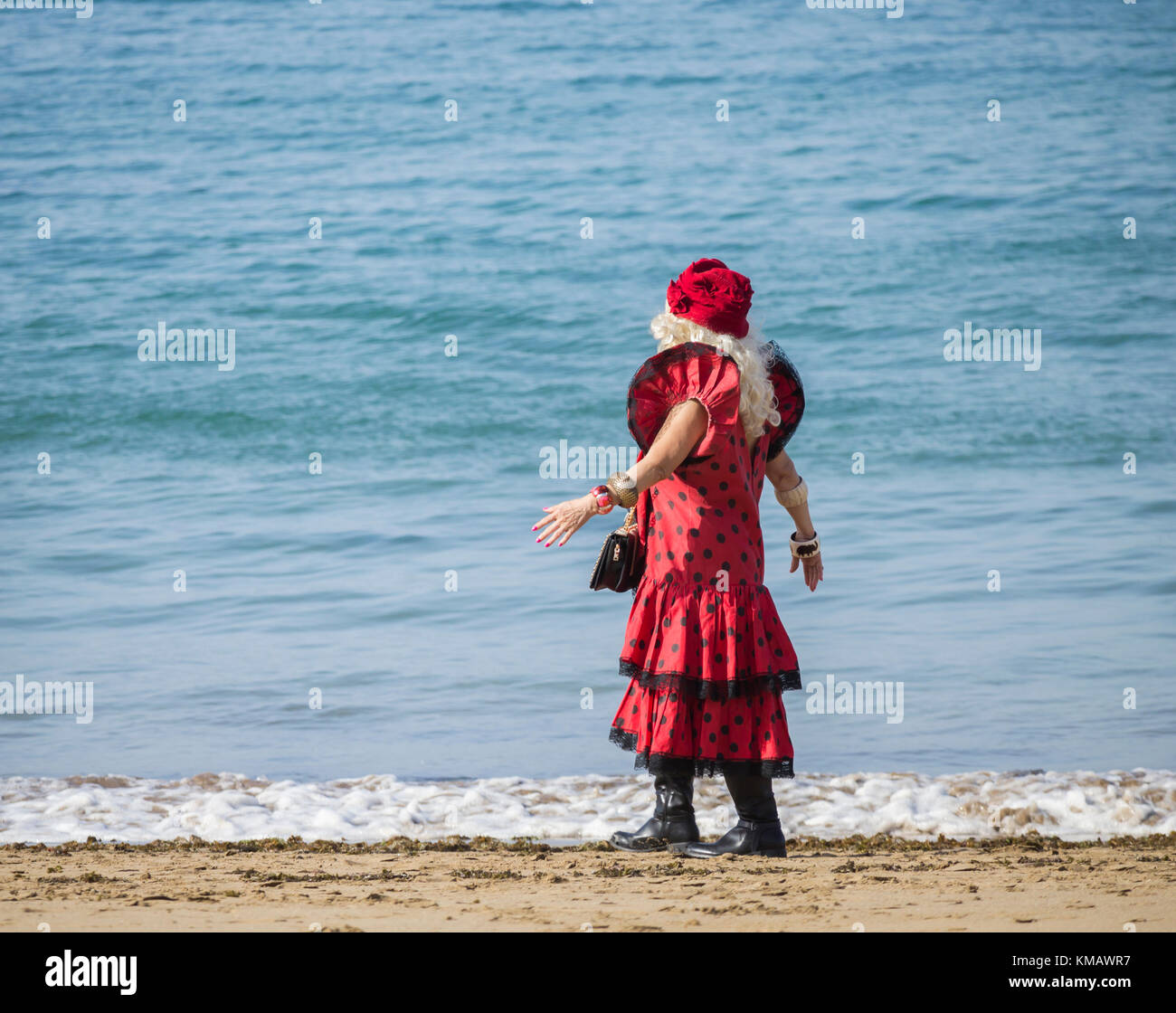 Eine ältere Frau mit rotem Flamenco-Kleid, die am Strand in spanien spaziert Stockfoto