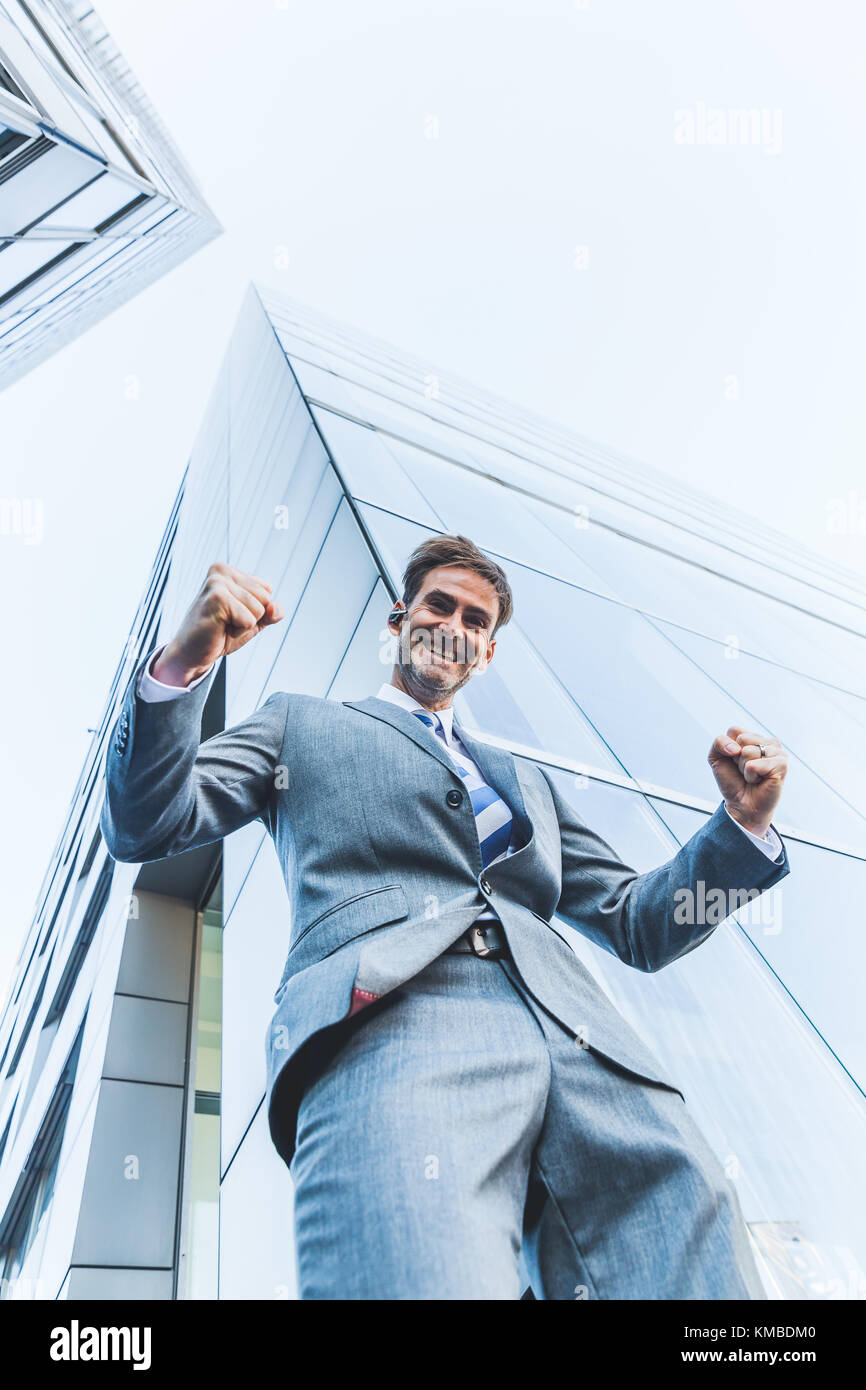 Bild von einem Geschäftsmann, der zwischen Wolkenkratzer steht und macht einen Gewinner Faust Stockfoto
