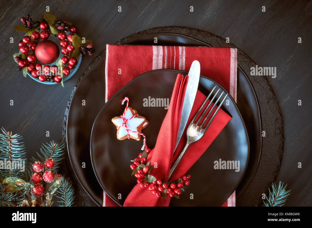 Weihnachtsmenü Konzept auf dunklem Hintergrund. Die schwarzen Platten und vintage Besteck mit Weihnachtsschmuck in Grün und Rot. Stockfoto