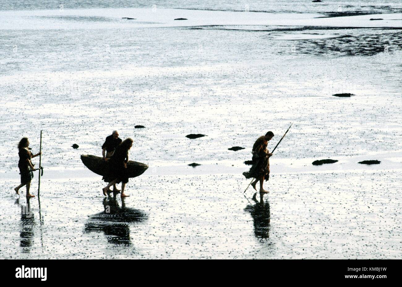 Neolithische Höhle Urmenschen Caveman Höhlenmenschen Mann zu Fuß auf Wattenmeer Küste tragen Haut Boot Coracle Curragh und Speere Stockfoto