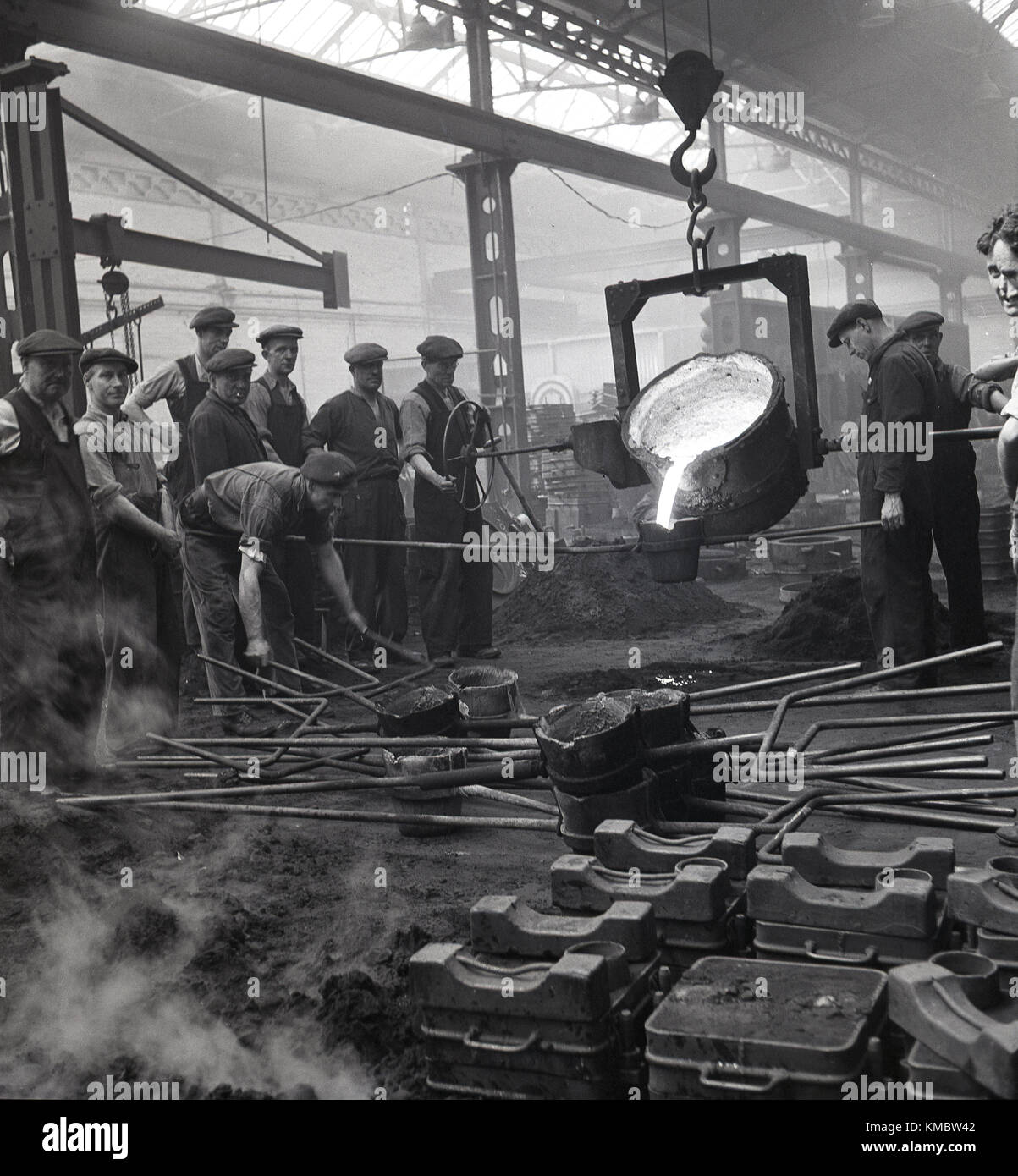 1950, historische, Schiffbau.... eine kleine Gruppe der männlichen Beschäftigten sammeln aound eine Eisen- und Stahlerzeugung geschmolzenen Ofen oder tiegel am Harland und Wolff Werft in Belfast, Nordirland. Beachten Sie, dass Tuch Kappen waren, was diese Zeit getragen wurde, nicht schwer hüten! Stockfoto