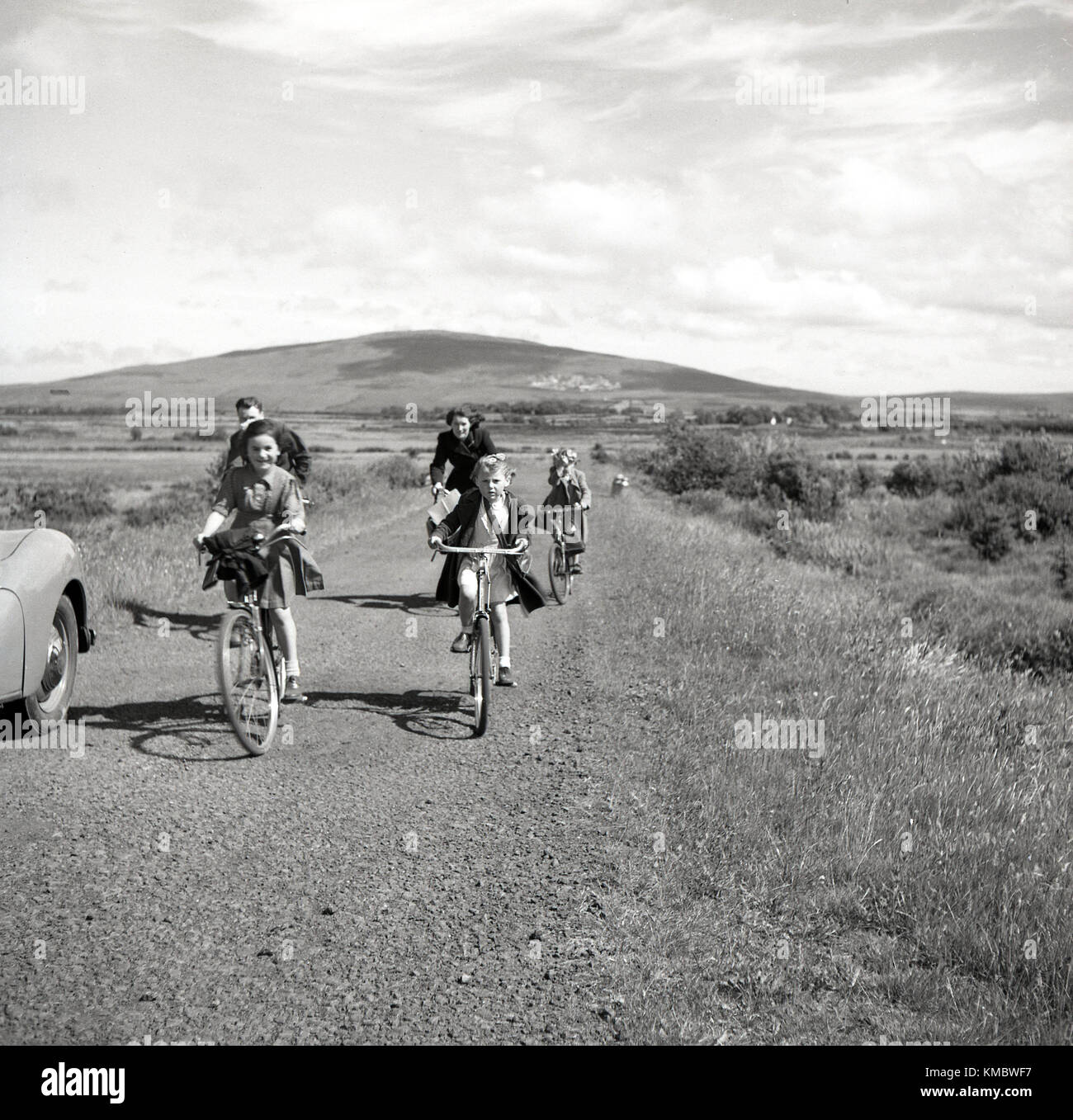 1950, historische, Mutter und Vater Radfahren mit ihren jungen Kindern entlang einer Landschaft, Nordirland. Sie sind entweder Verwandte zu besuchen oder vielleicht eine Kirche als Mädchen zu besuchen, sind alle Kleider tragen. Stockfoto