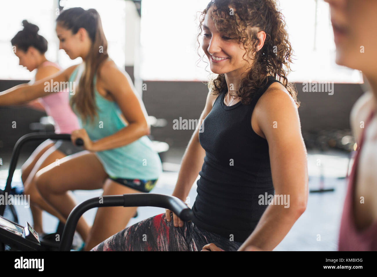 Lächelnde junge Frau Reiten elliptischen Fahrrad in Übung Klasse Stockfoto