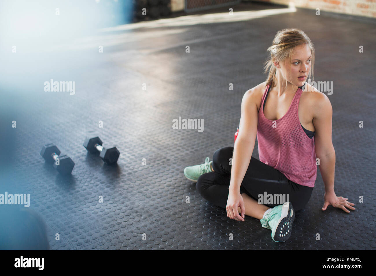 Junge Frau, die sich streckt, sich im Fitnessstudio neben den Hanteln dreht Stockfoto