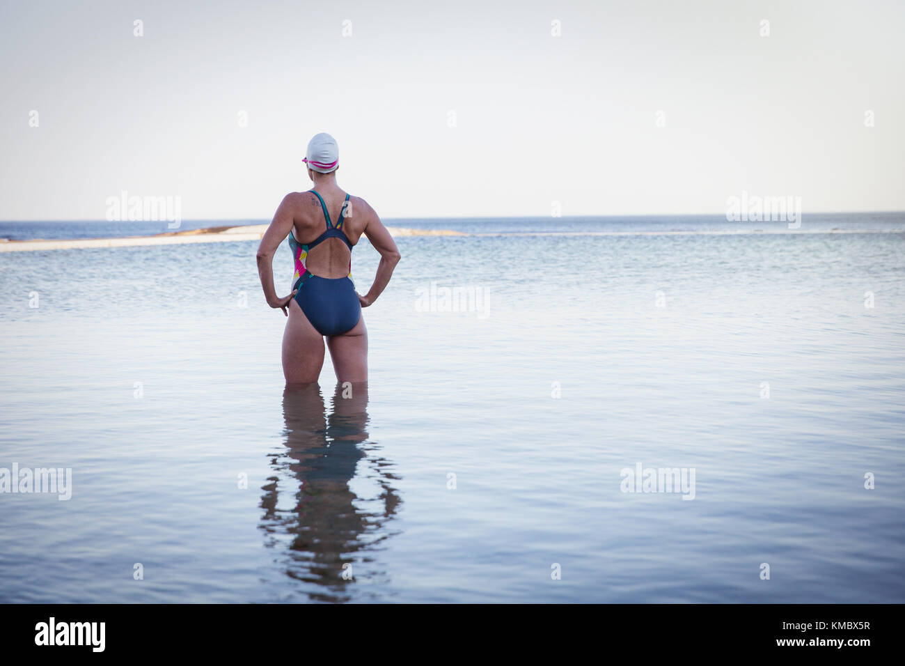 Nachdenkliche, entschlossene Schwimmerin mit Händen an den Hüften in der Ozeanbrandung Stockfoto