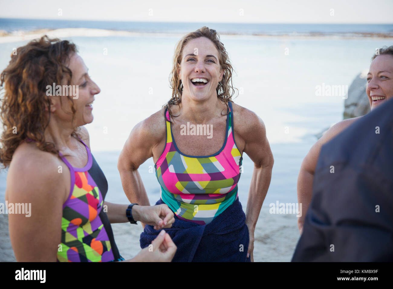 Lachende Schwimmerinnen im offenen Wasser, die am Meeresstrand reden Stockfoto