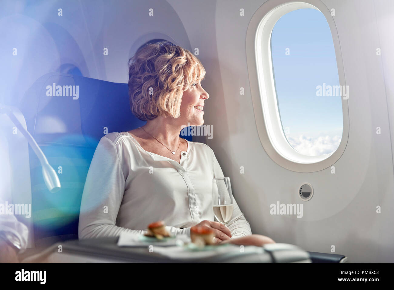 Lächelnde Frau, die Champagner trinkt, First Class reist und aus dem Flugzeugfenster schaut Stockfoto
