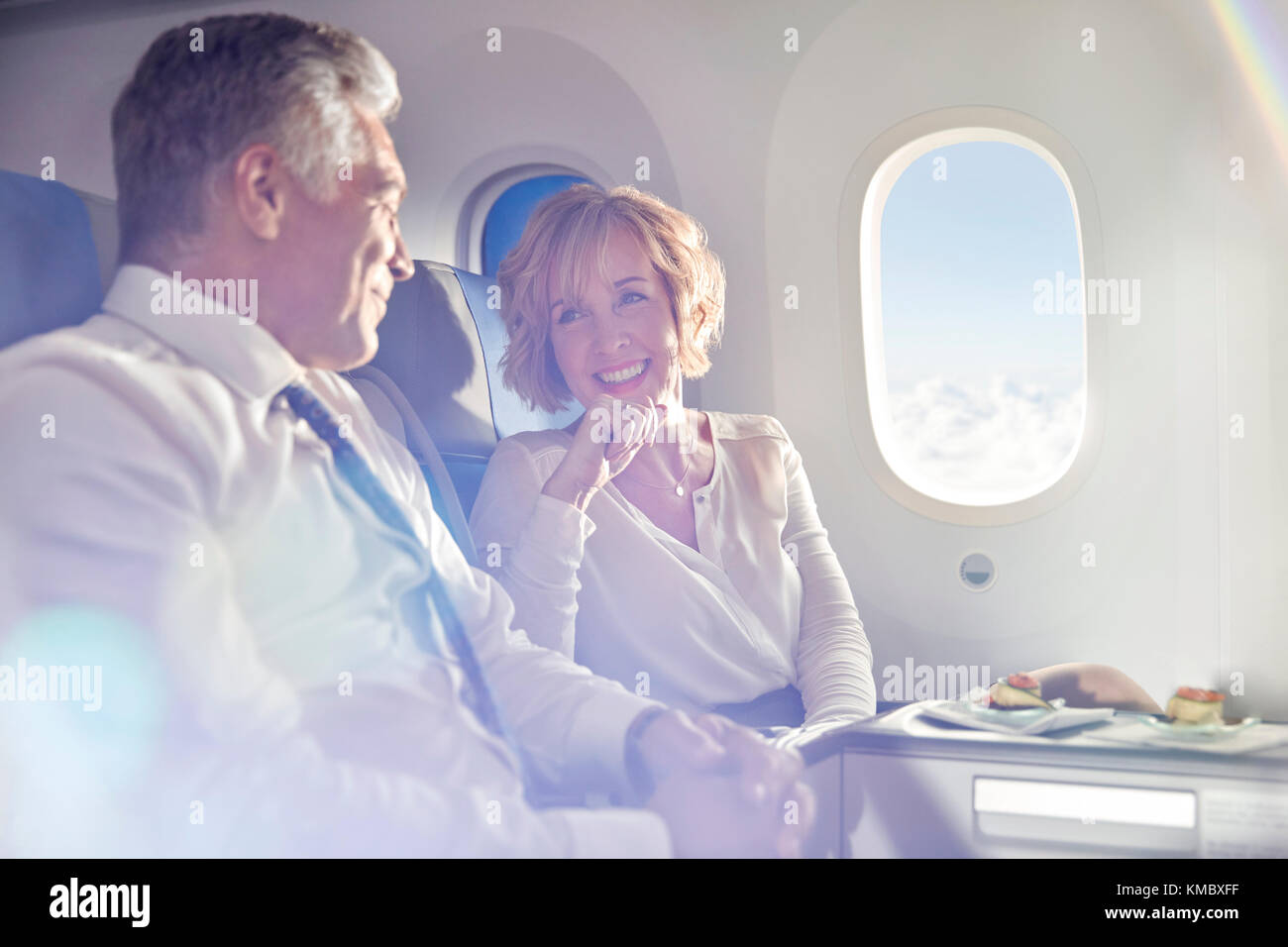 Lächelndes reifes Paar, das in erster Klasse isst und spricht Flugzeug Stockfoto