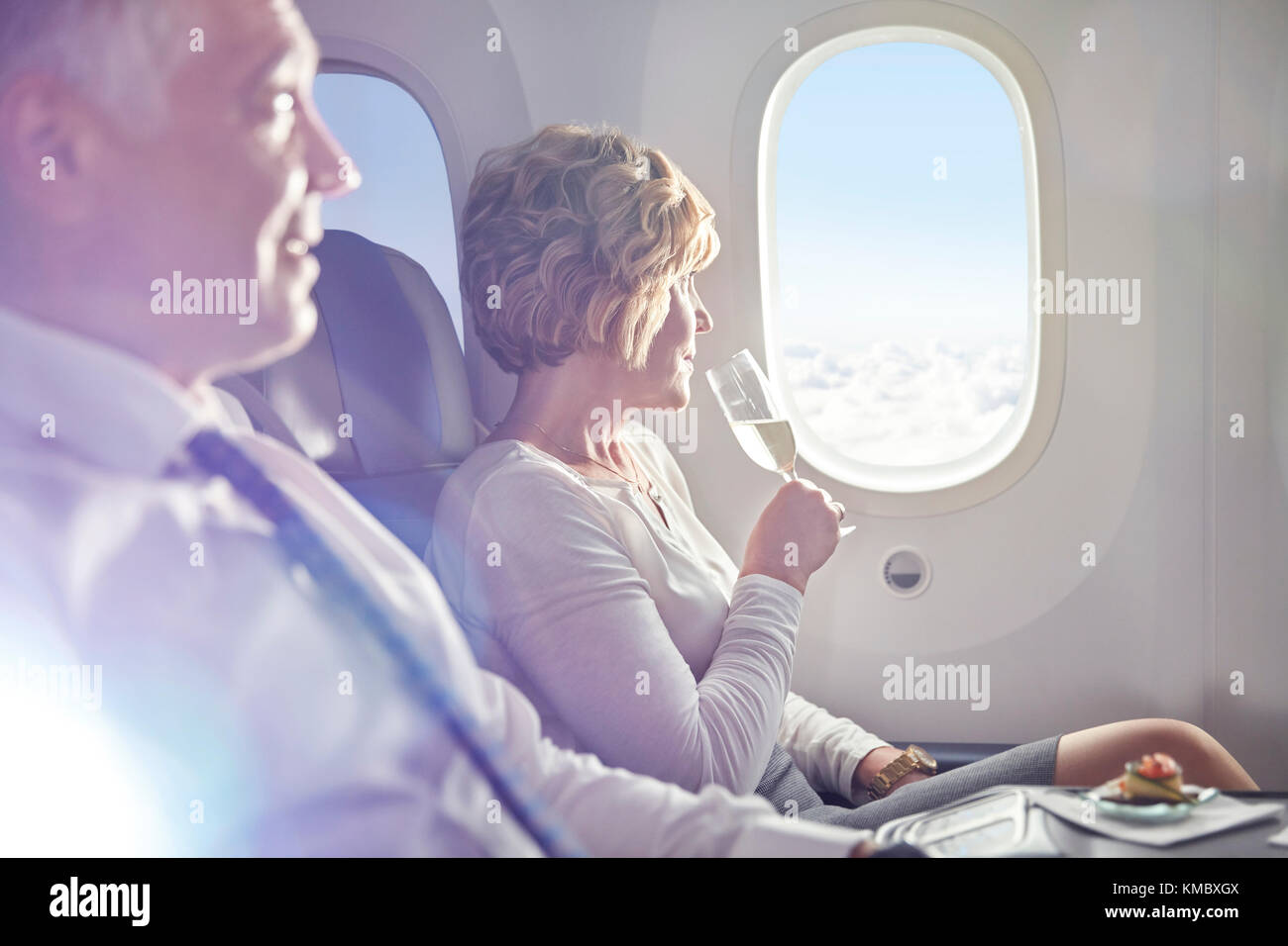 Frau trinkt Champagner in erster Klasse und blickt aus dem Flugzeugfenster Stockfoto