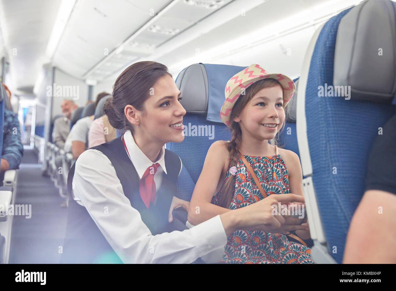 Weibliche Flugbegleiterin hilft Mädchen im Flugzeug Stockfoto