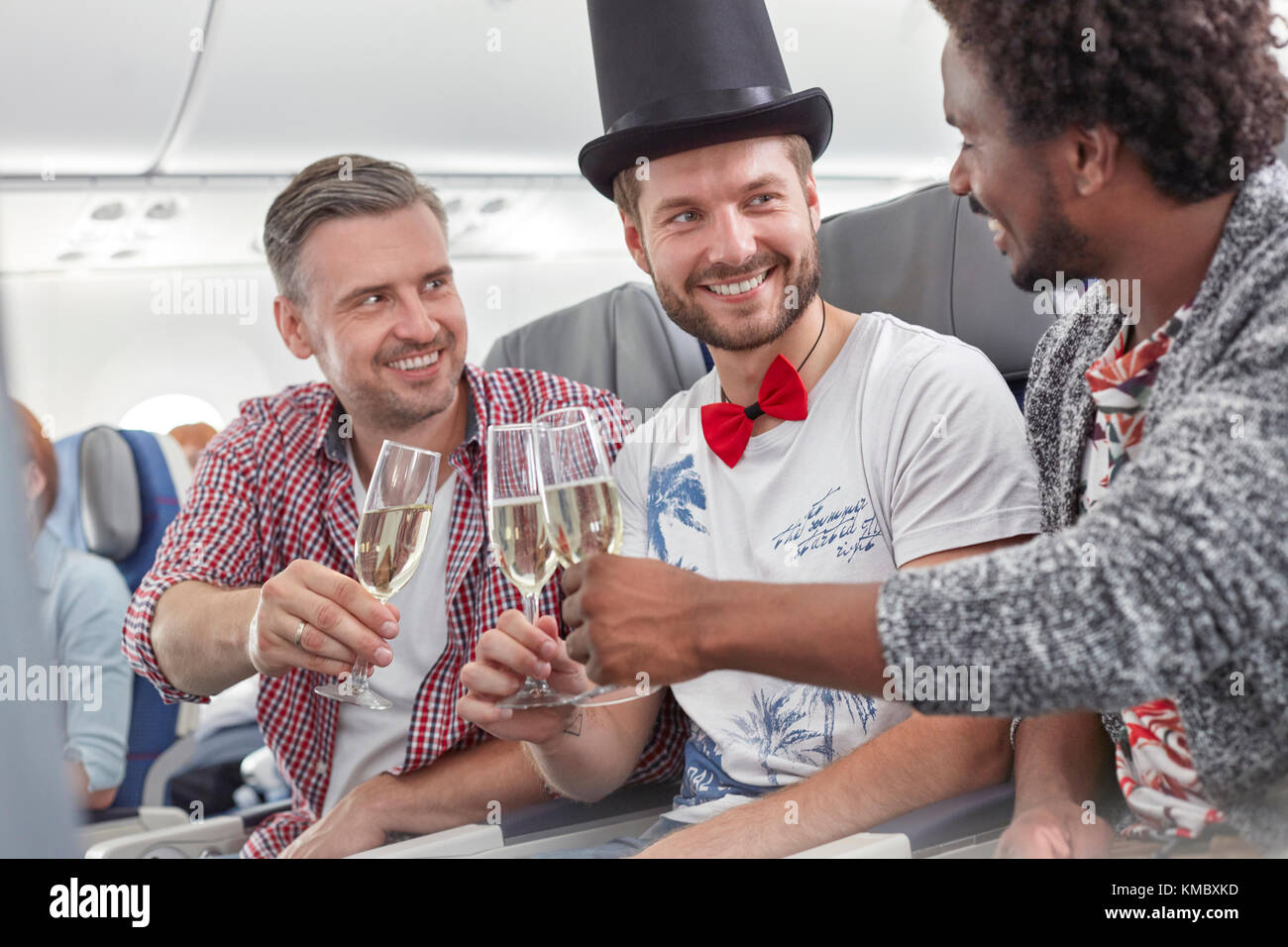Junge männliche Freunde toasten Sektgläser im Flugzeug Stockfoto