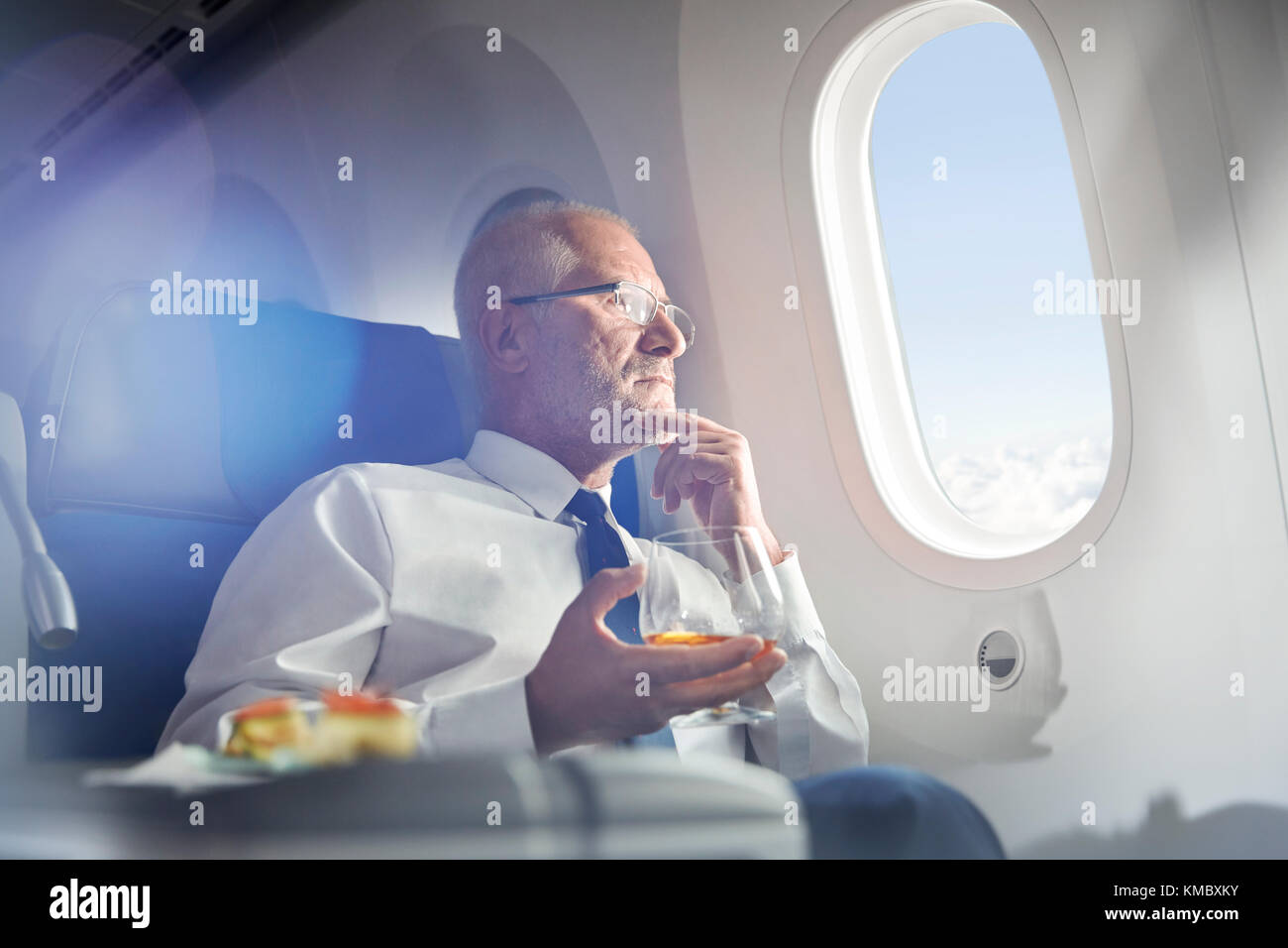 Ein älterer Geschäftsmann trinkt Whisky in erster Klasse und blickt aus dem Flugzeugfenster Stockfoto