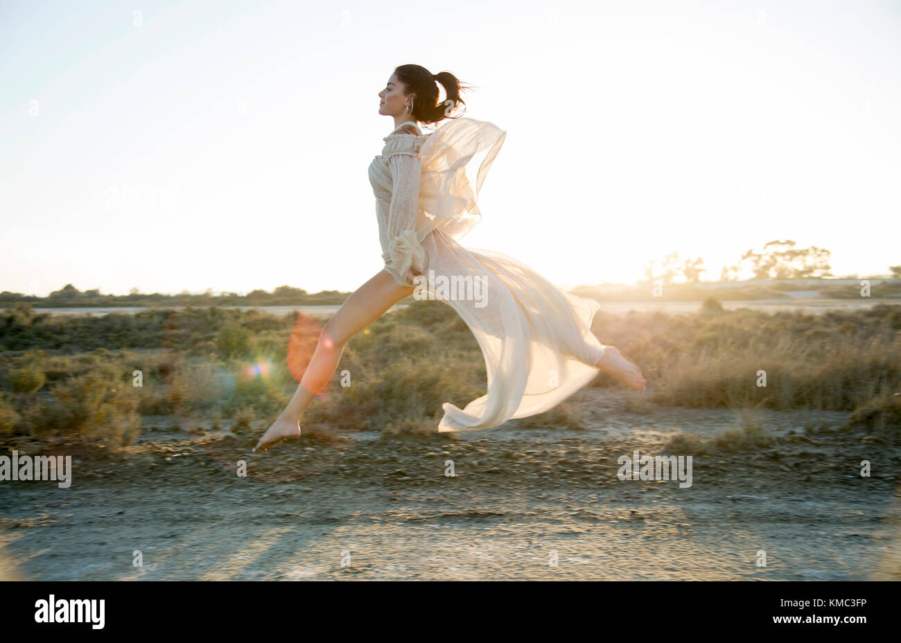 Mädchen, die bei Sonnenuntergang in einem weißen Feld springen Kleid Stockfoto