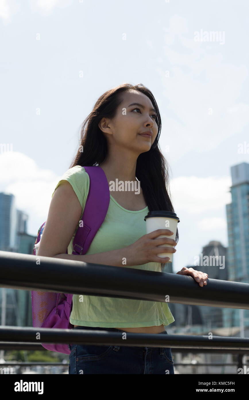 Asiatische Frau mit einer Kaffeetasse, die in der Nähe des Geländer steht Stockfoto