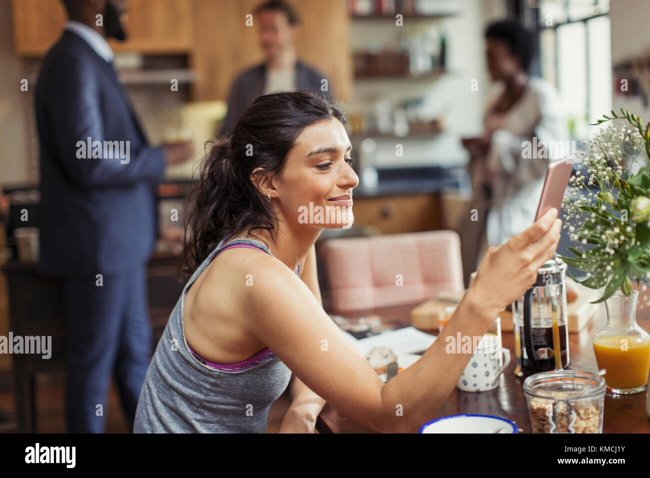 Junge Frau, die am Frühstückstisch mit einem Smartphone schreibt Stockfoto