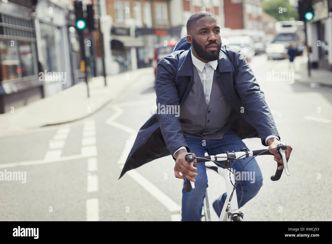 Junger männlicher Geschäftsmann pendelt auf dem Fahrrad auf der sonnigen städtischen Straße Stockfoto