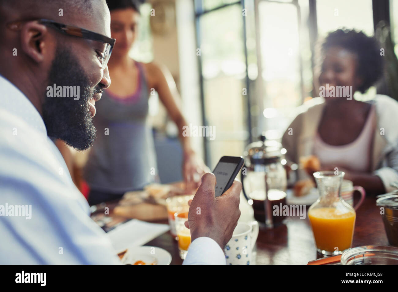 Junger Mann, der mit Smartphone am Küchentisch schreibt Stockfoto