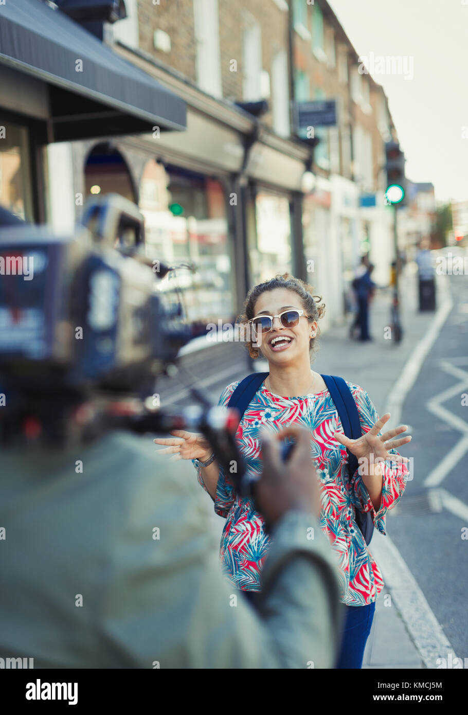 Enthusiastische junge Frau posiert für Videokamera auf städtischen Straße Stockfoto