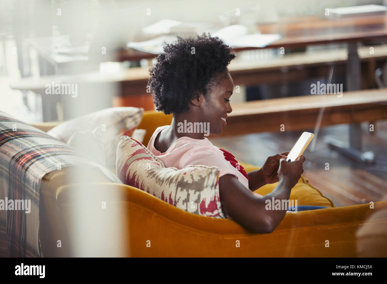 Lächelnde Frau, die mit einem Smartphone auf dem Sofa im Wohnzimmer schreibt Stockfoto