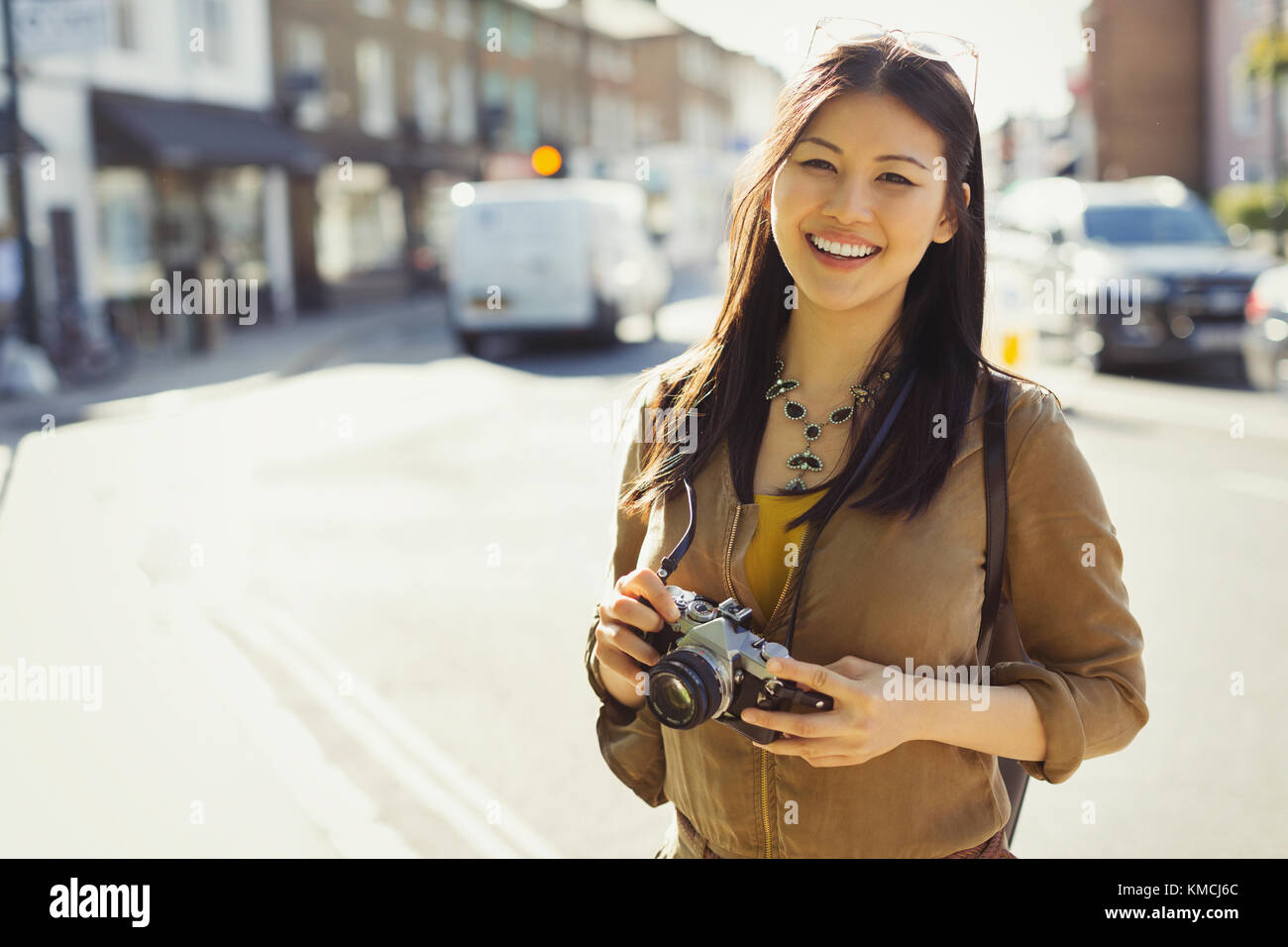 Portrait lächelnd, selbstbewusst junge Tourist mit Kamera auf sonnigen städtischen Straße Stockfoto