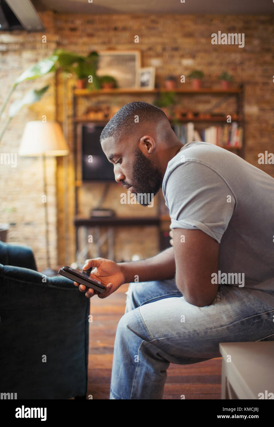 Junger Mann SMS mit Smartphone im Wohnzimmer Stockfoto
