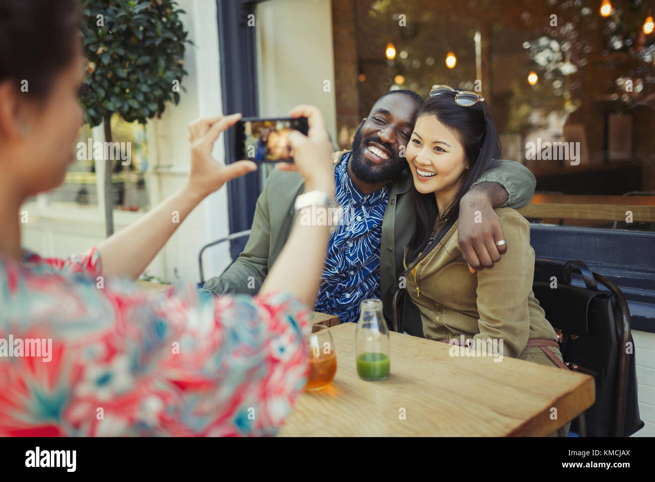 Frau fotografiert liebevolle paar Freunde mit Kamera-Handy auf Bürgersteig Café Stockfoto