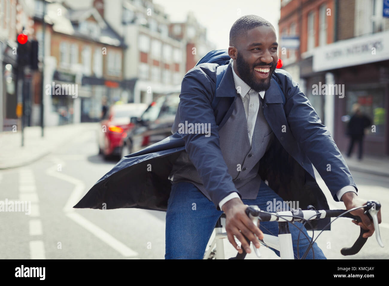 Lächelnder junger Geschäftsmann pendelt, Fahrrad auf sonniger Stadtstraße reitet Stockfoto