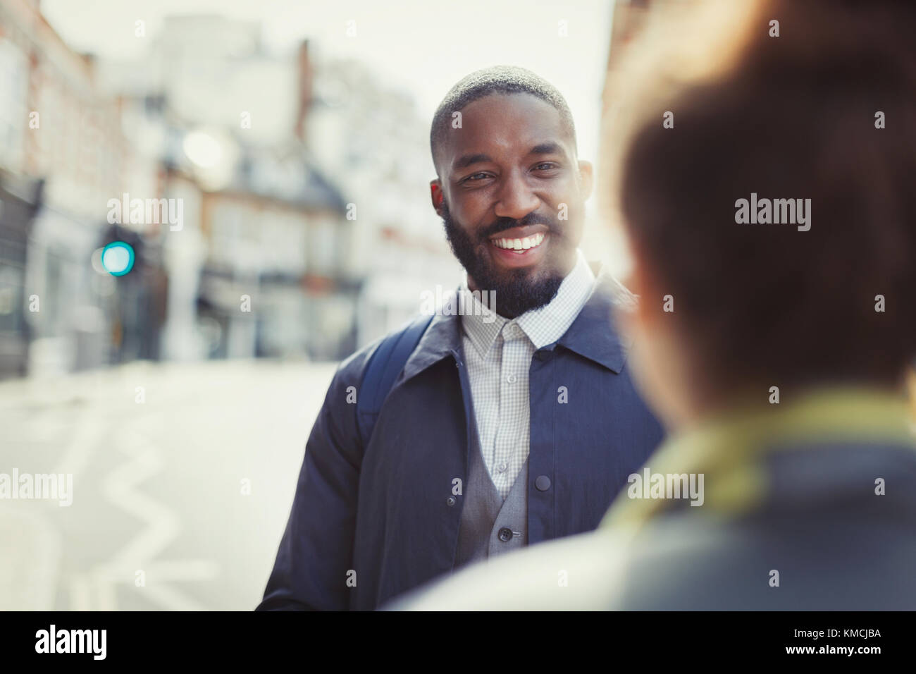 Lächelnder Geschäftsmann im Gespräch mit einem Freund auf der sonnigen städtischen Straße Stockfoto