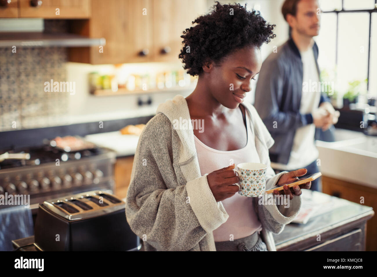 Frau trinkt Kaffee, SMS mit Smartphone in der Küche Stockfoto