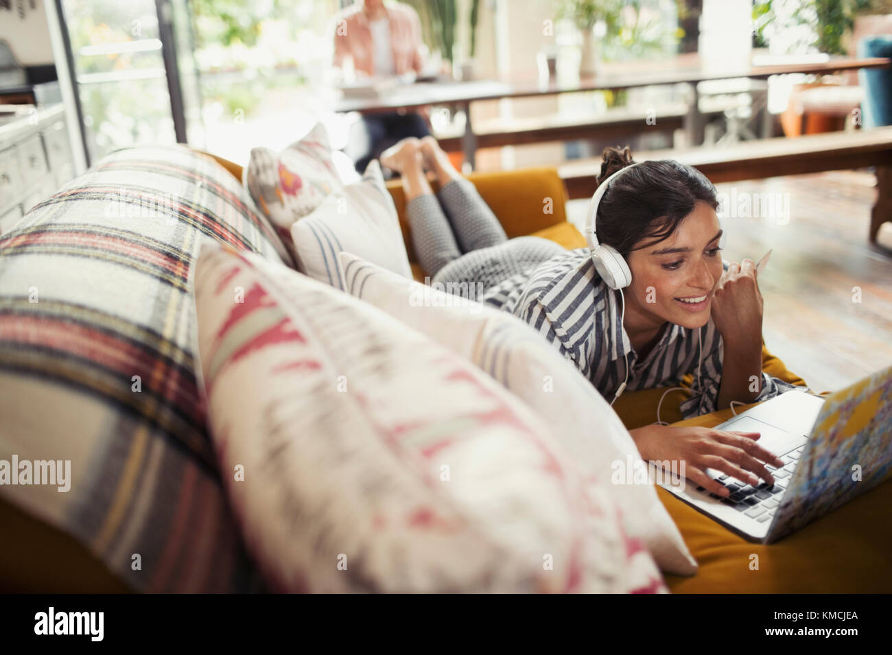 Lächelnde Frau mit Kopfhörern mit Laptop auf dem Sofa Stockfoto