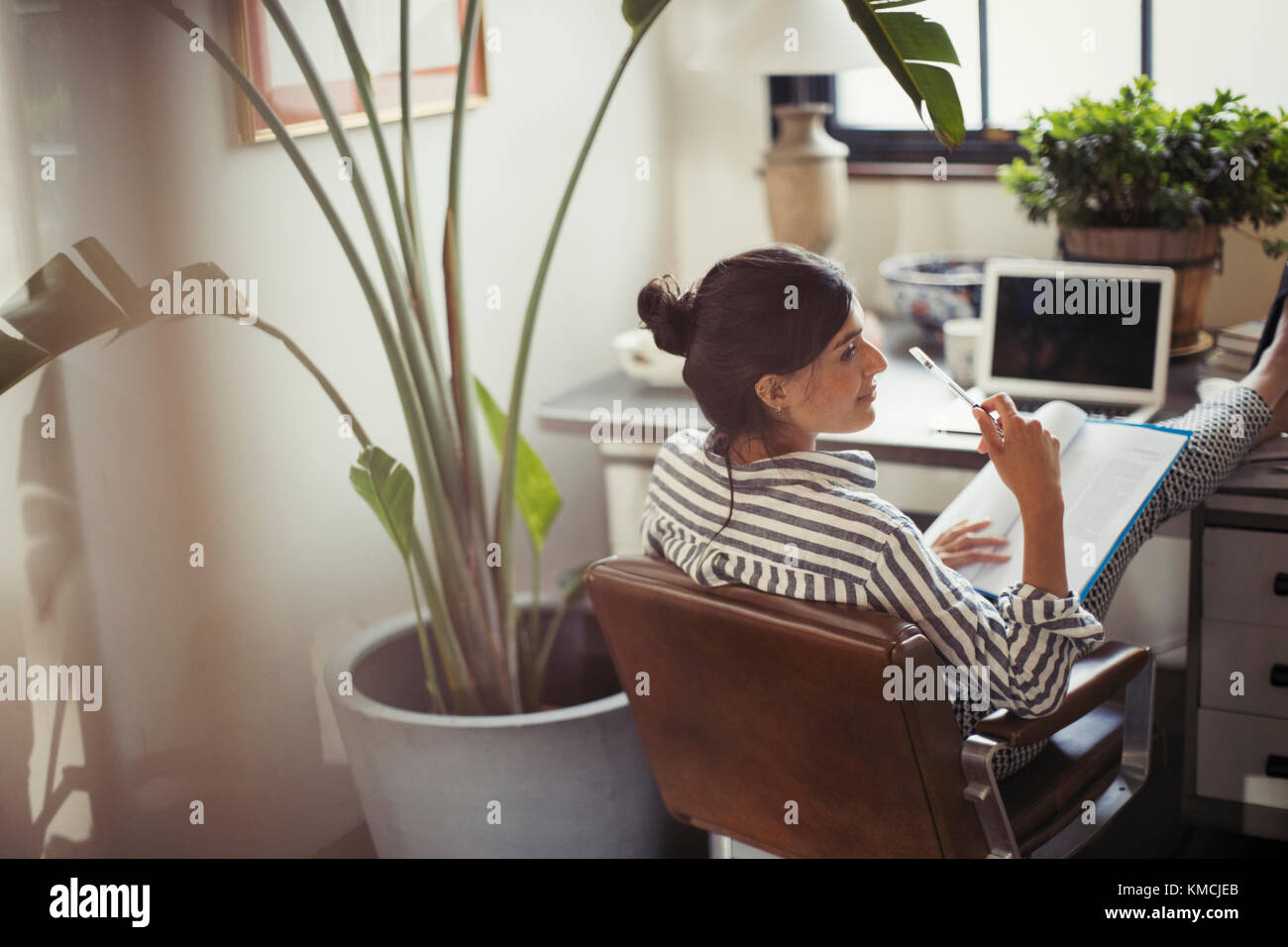 Geschäftsfrau liest Schreibarbeit mit den Füßen auf dem Schreibtisch Stockfoto