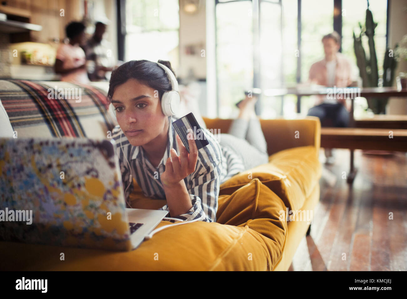 Junge Frau mit Kopfhörer und Kreditkarte Online-Shopping bei Laptop auf Wohnzimmersofa Stockfoto