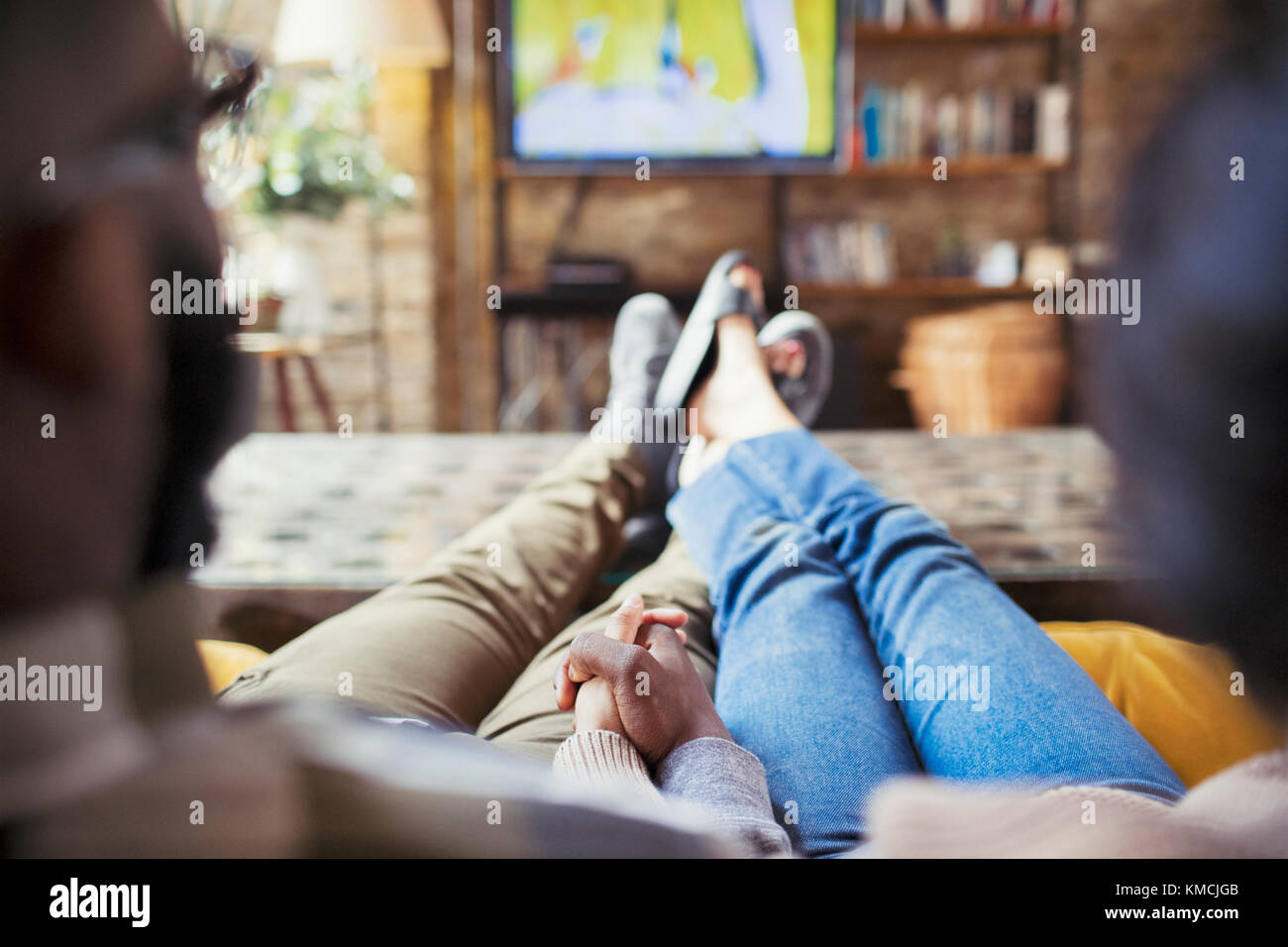 Zärtliches Paar, das die Hände hält und im Wohnzimmer Fernsehen sieht Stockfoto
