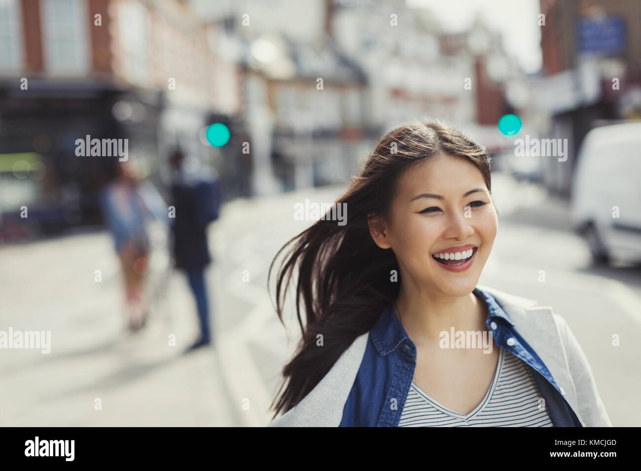 Lächelnde, enthusiastische junge Frau, die auf der sonnigen Stadtstraße läuft Stockfoto